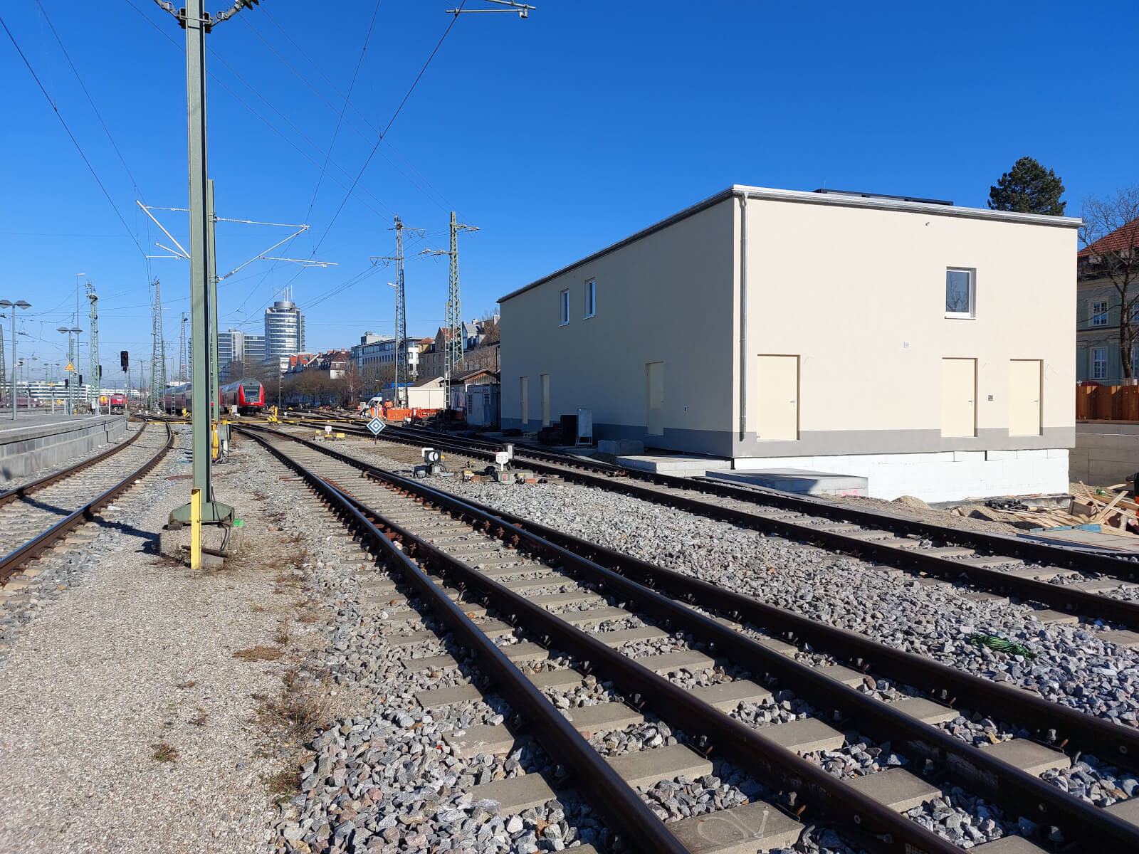 Rechts von einer Bahnstrecke steht ein graues, kastenförmiges Technikgebäude
